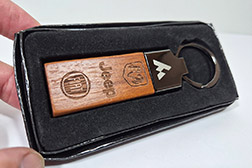 Llavero de diseño contemporáneo y elegante modelo Delta. Combina un cuerpo metálico con un acabado pulido estilo gunmetal (negro niquelado) y una inserción de madera de veta rica y coloración rojiza. Su perfil rectangular es limpio y sofisticado. Las medidas exactas son 7,5 cm de largo, 2,2 cm de ancho y 0,8 cm de espesor. Este llavero ofrece una superficie excepcional para la personalización de alta precisión mediante grabado láser tanto en la parte de madera como en la parte metálica, permitiendo que su marca o logotipo se destaque con gran detalle. El metal gunmetal proporciona durabilidad y un toque moderno, mientras que la madera añade calidez y un tacto natural. Cada unidad presenta una textura de veta única y un acabado impecable. Es un artículo excelente para regalos corporativos premium y merchandising de lujo. - 2